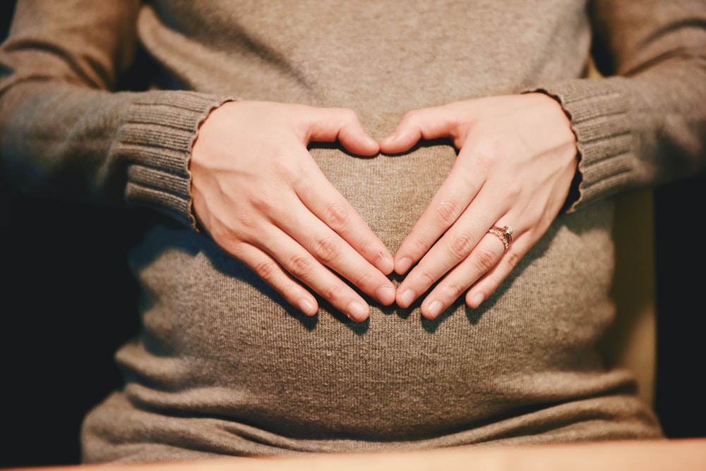 woman making a heart shape with her hands on her pregnant belly